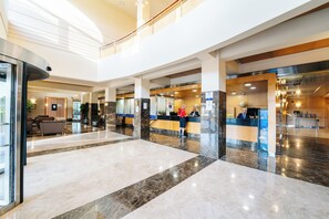 Un vestíbulo amplio con mostrador de recepción, zona de estar y una escalera que conduce a un nivel superior.