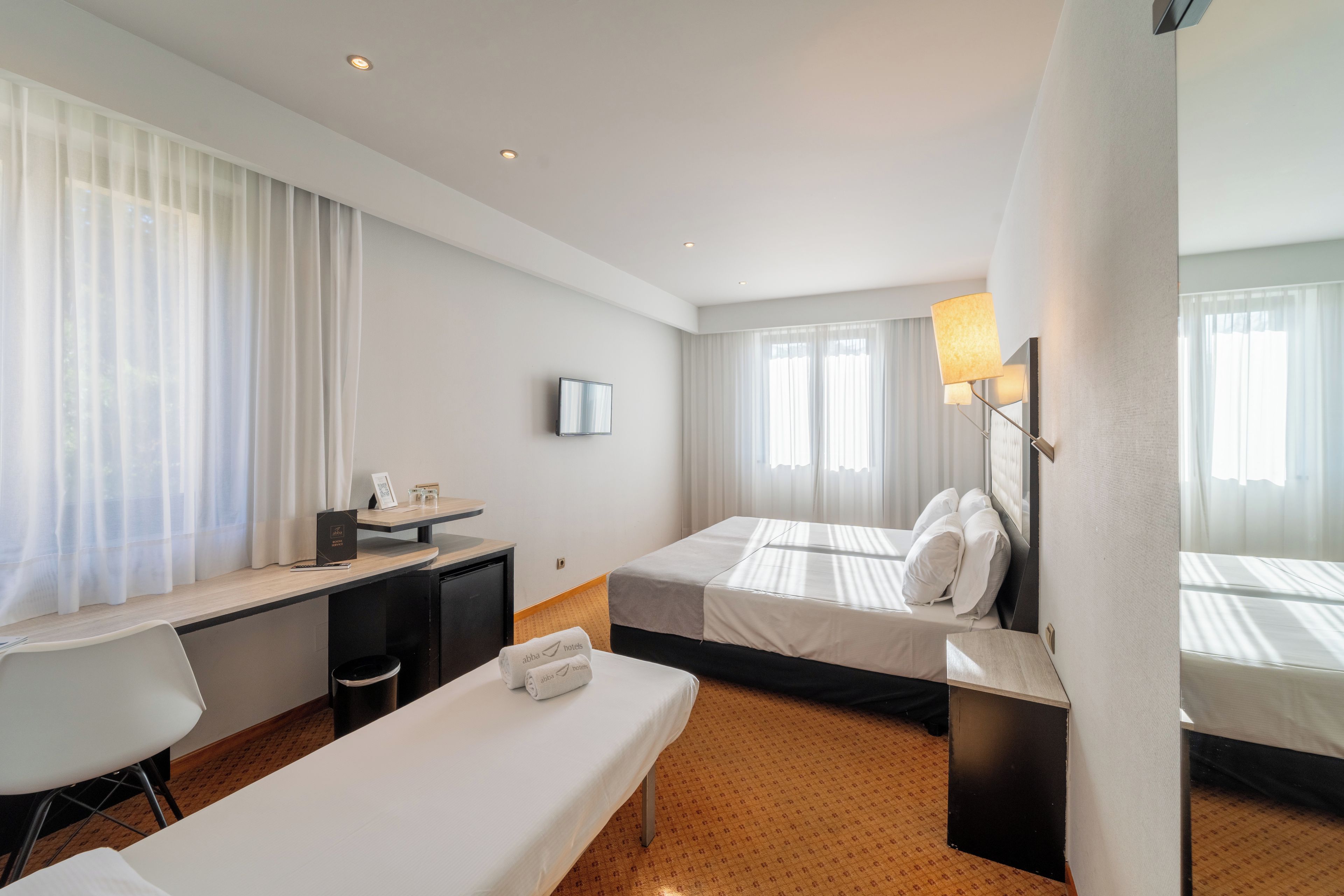 Ett hotellrum med två sängar, ett skrivbord, en stol, en TV och ett fönster med gardiner.