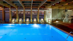 Ein Schwimmbecken mit gefliestem Boden und Liegestühlen aus Holz.