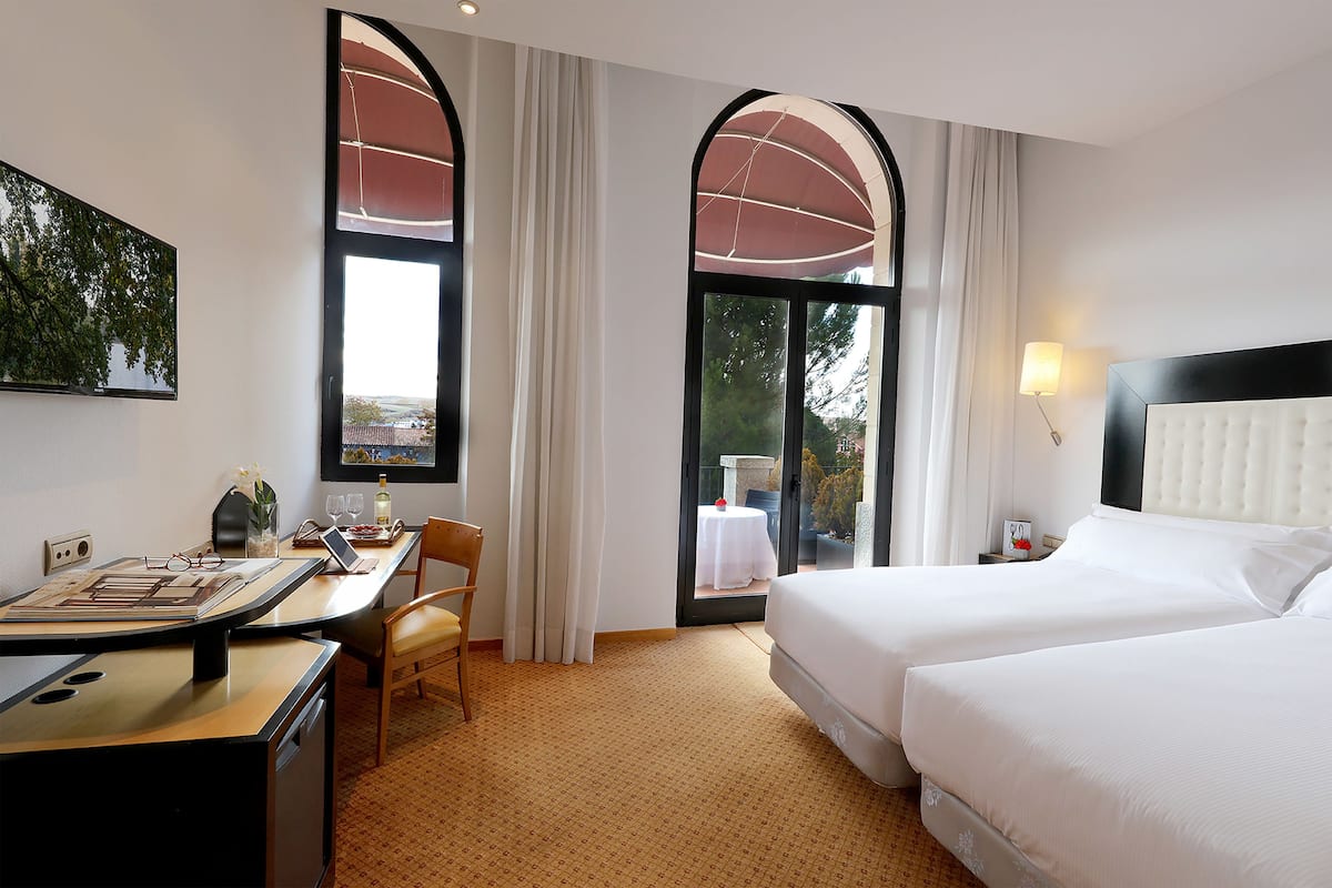 Habitació d'hotel amb dos llits, una escriptori amb un portàtil, una cadira i vista a l'exterior a través de grans finestres.