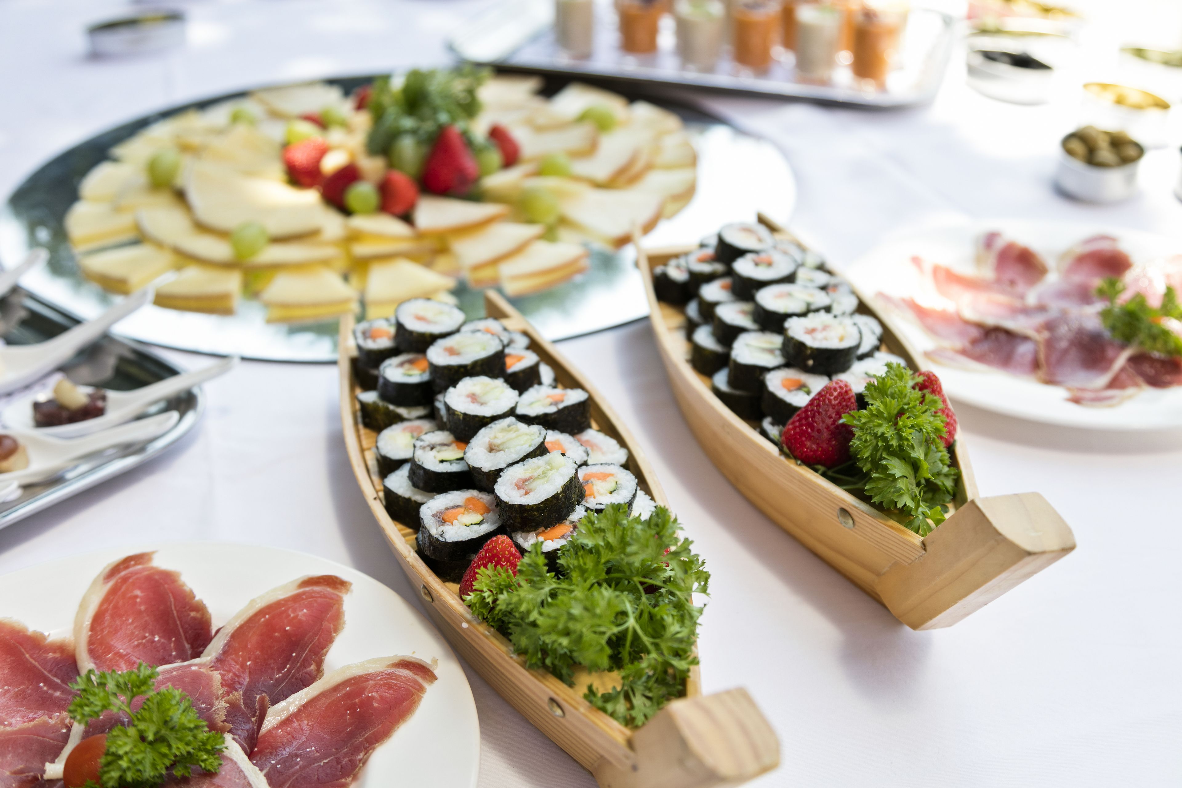 A buffet table with various food items including sushi, fruits, and meats.