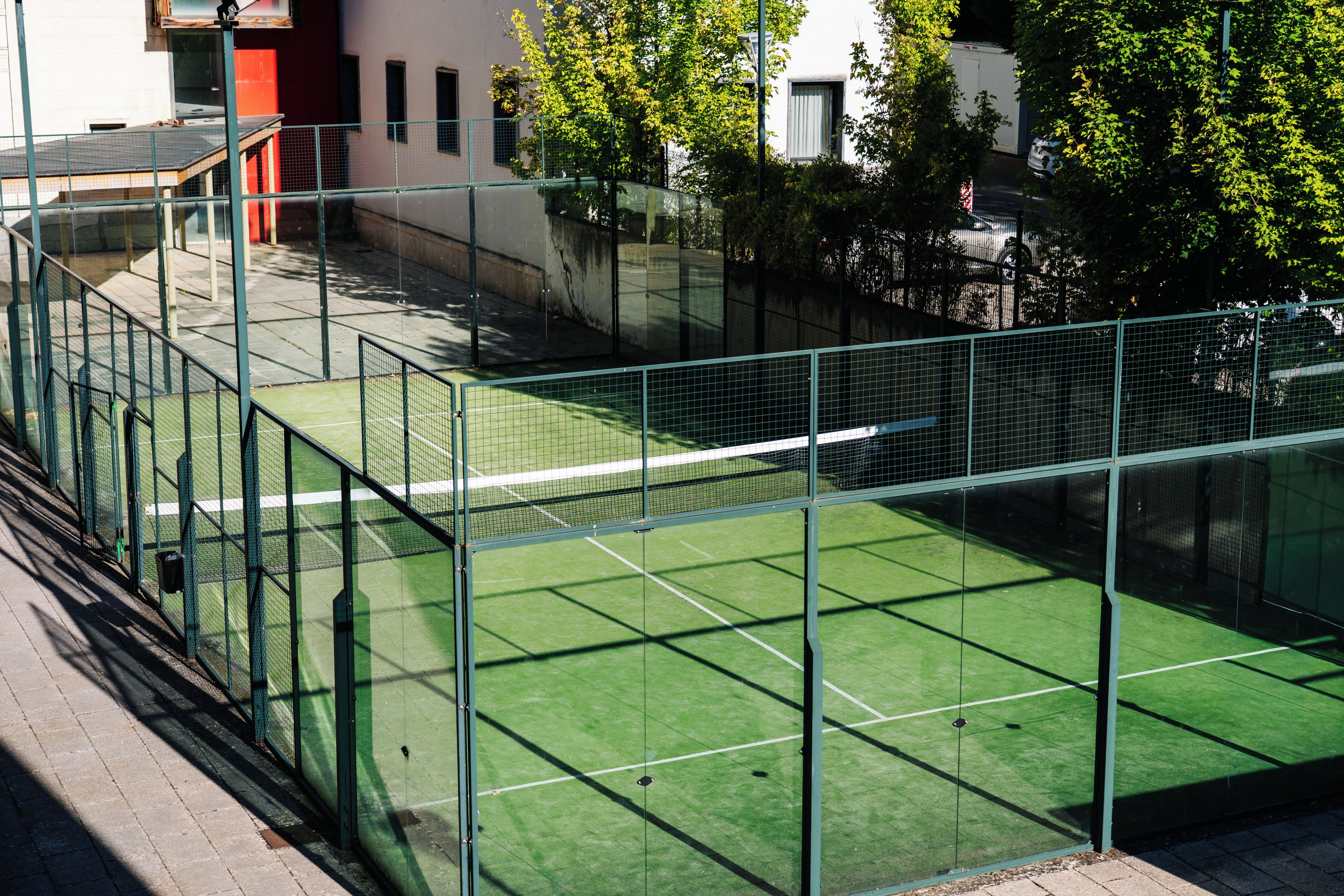 En tennisbana omgiven av ett grönt staket, med en byggnad i bakgrunden.