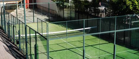 A tennis court enclosed by a green fence with a building in the background.