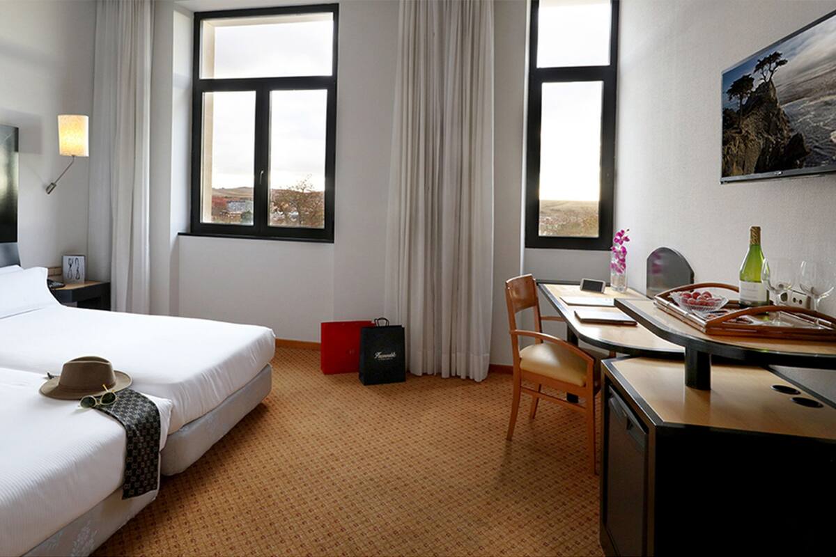 Habitació d'hotel amb dos llits, una taula de treball, una cadira, televisió i finestra amb vistes.