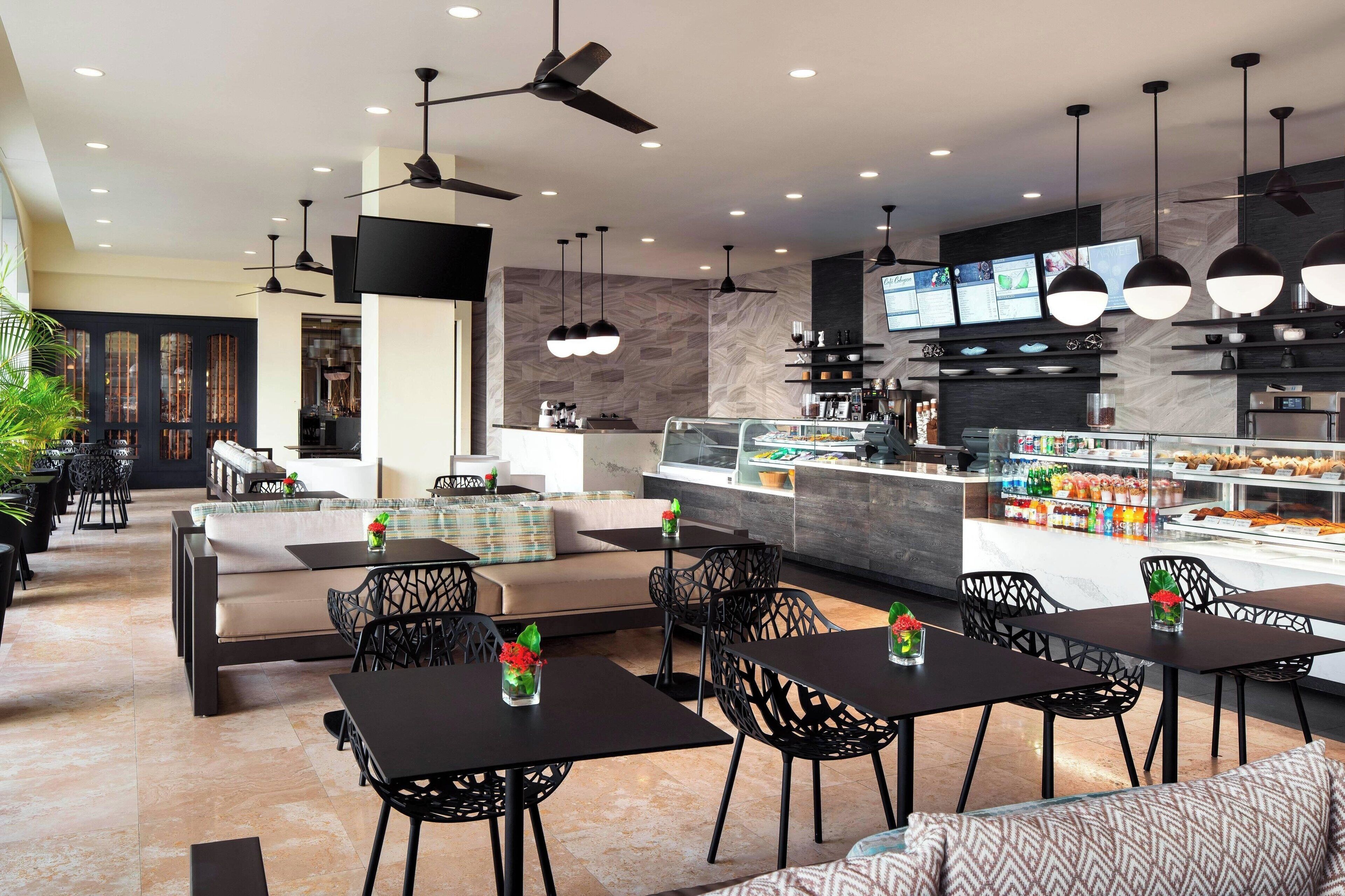A modern restaurant with black tables and chairs, a counter with a display case, and ceiling fans.