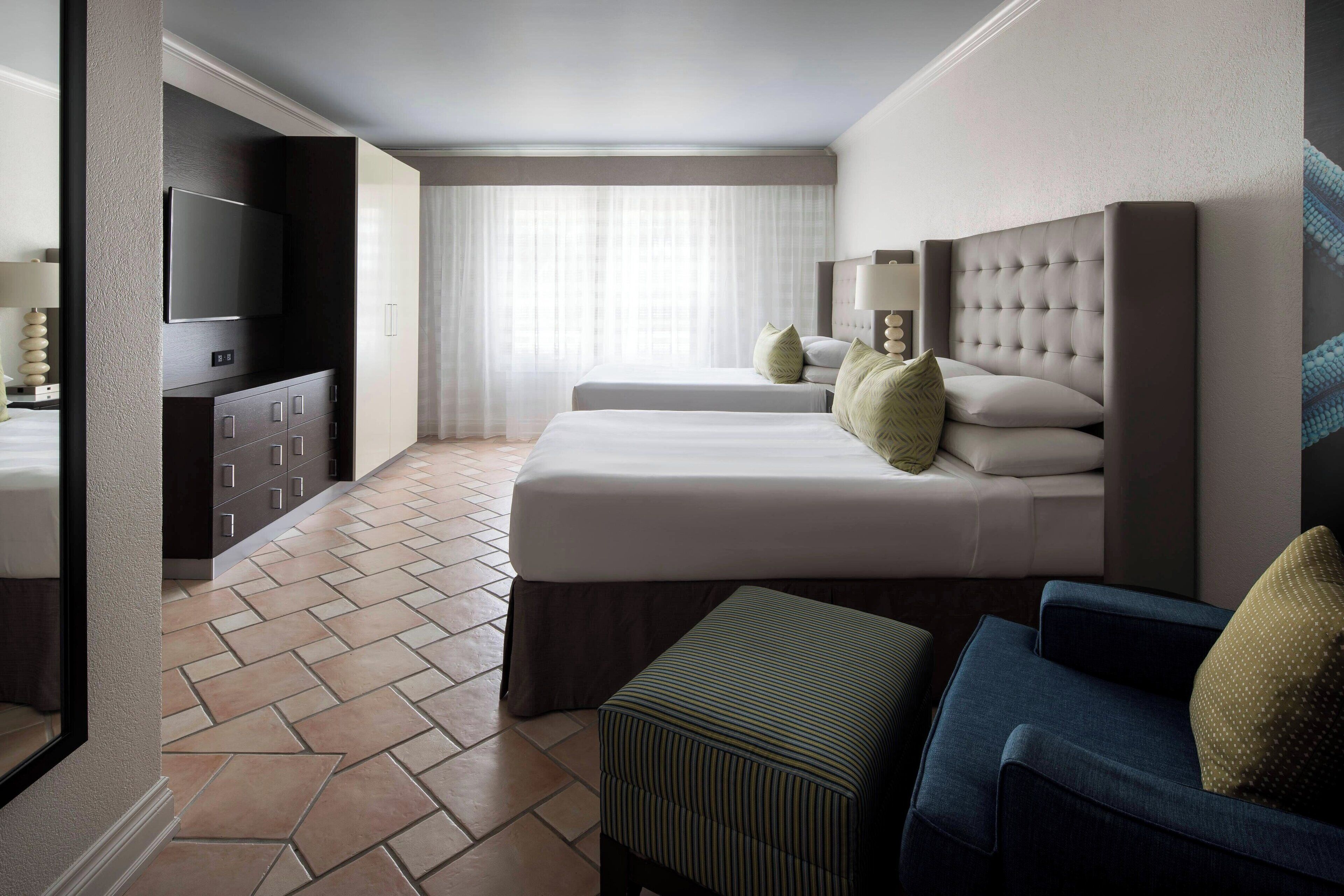 A hotel room with a large bed, a smaller bed, a TV, a desk, and a window with curtains.