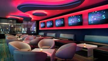 A modern lounge with curved ceiling lights, multiple seating areas, and digital screens displaying the lounge's name.