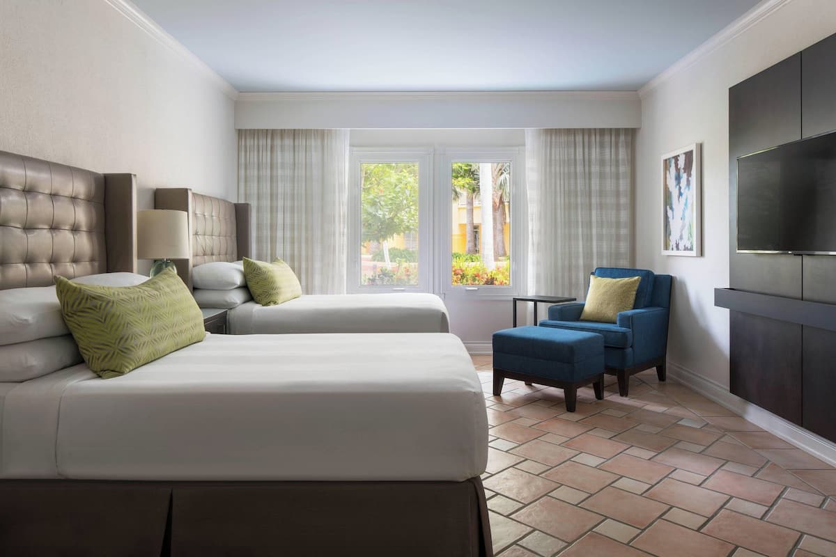 A hotel room with two beds, a TV, a chair, and a window with curtains.