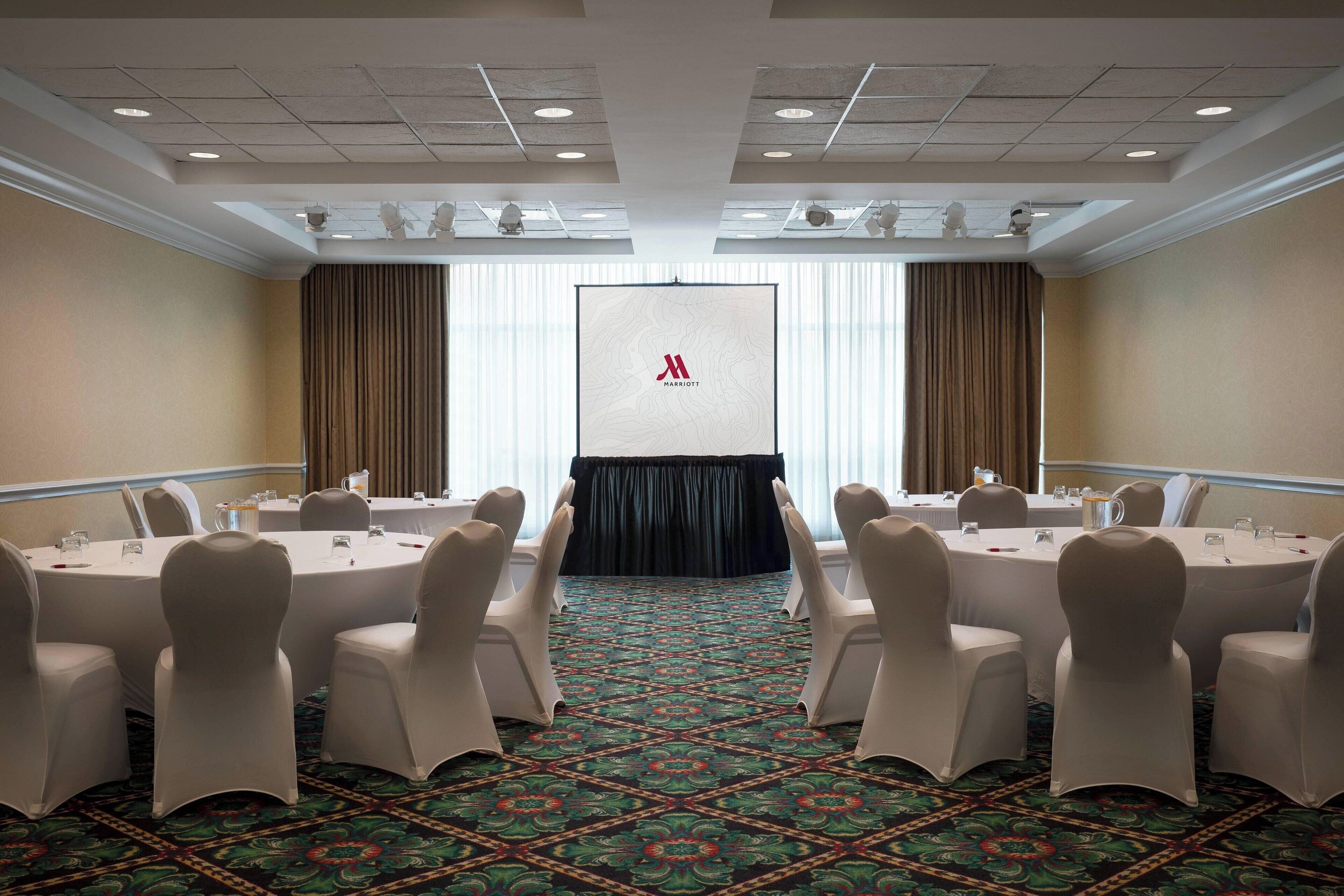 Une salle de conférence dotée d’un grand écran à l’avant, de tables rondes et de chaises.