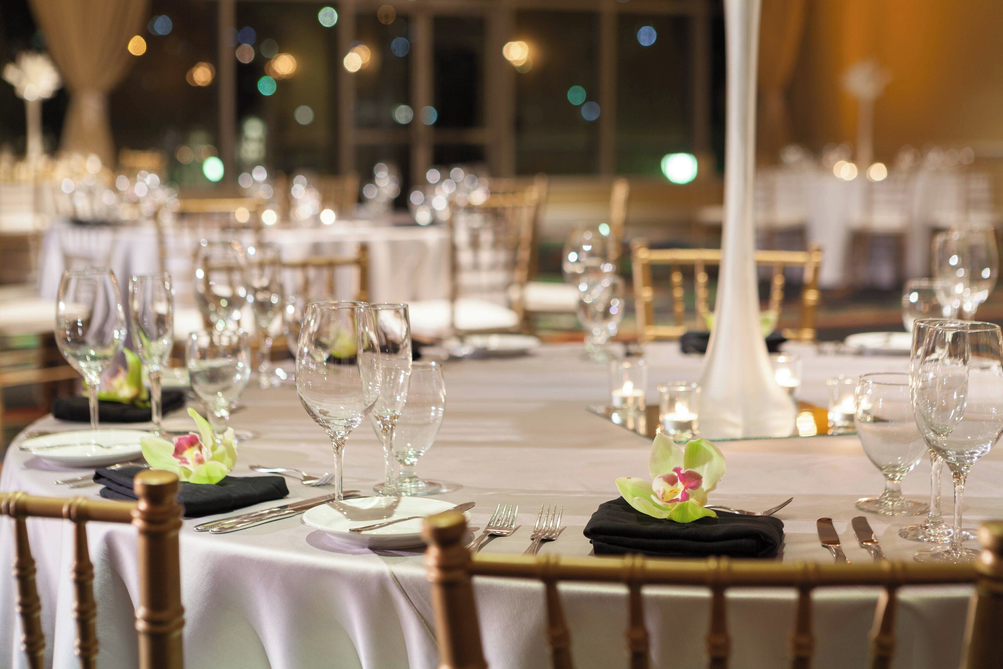 A banquet hall with round tables set for a formal event, featuring white tablecloths, clear glassware, and floral centerpieces.