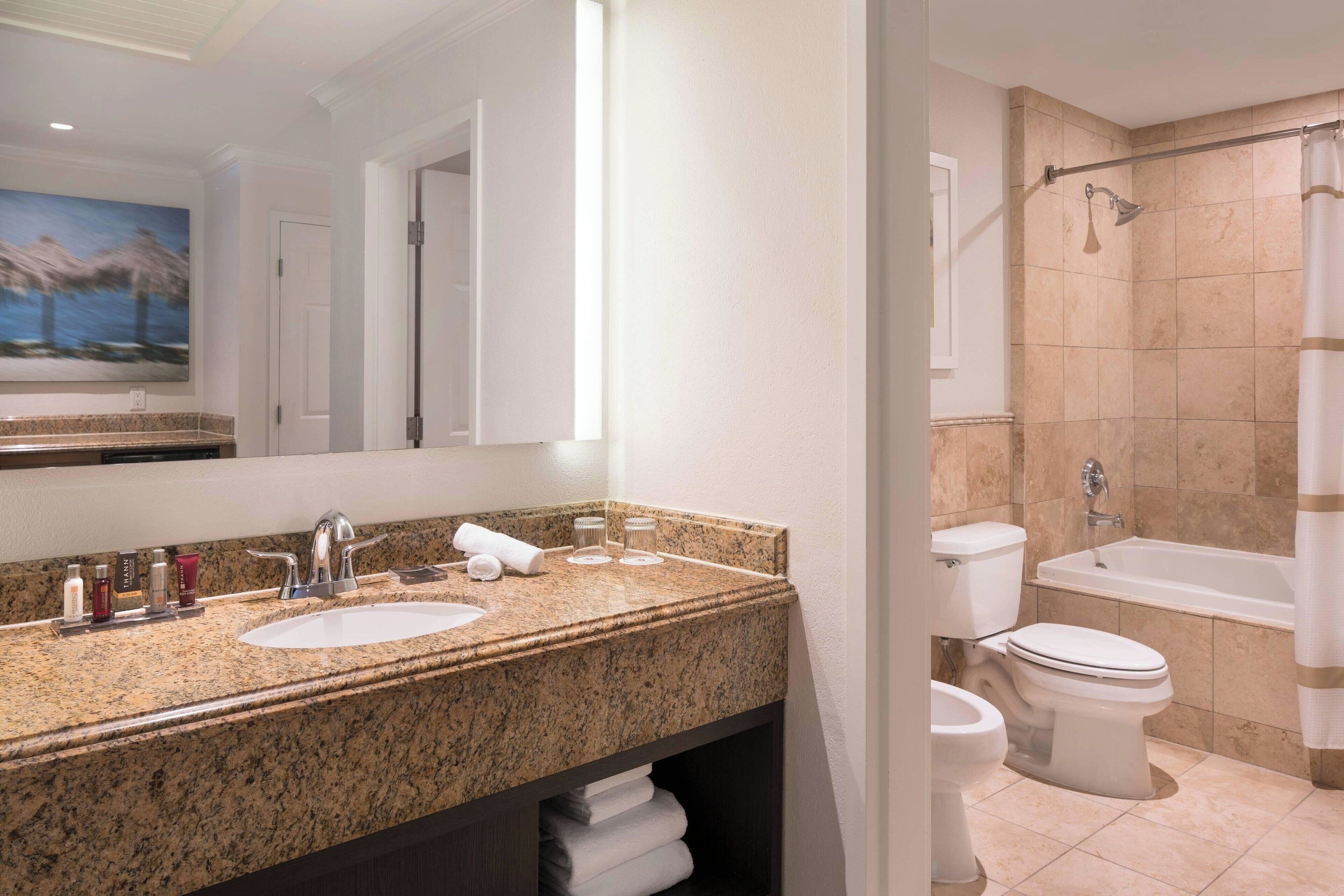 Un baño moderno con encimera de granito, dos lavamanos, un espejo grande, ducha con puerta de cristal y un inodoro.