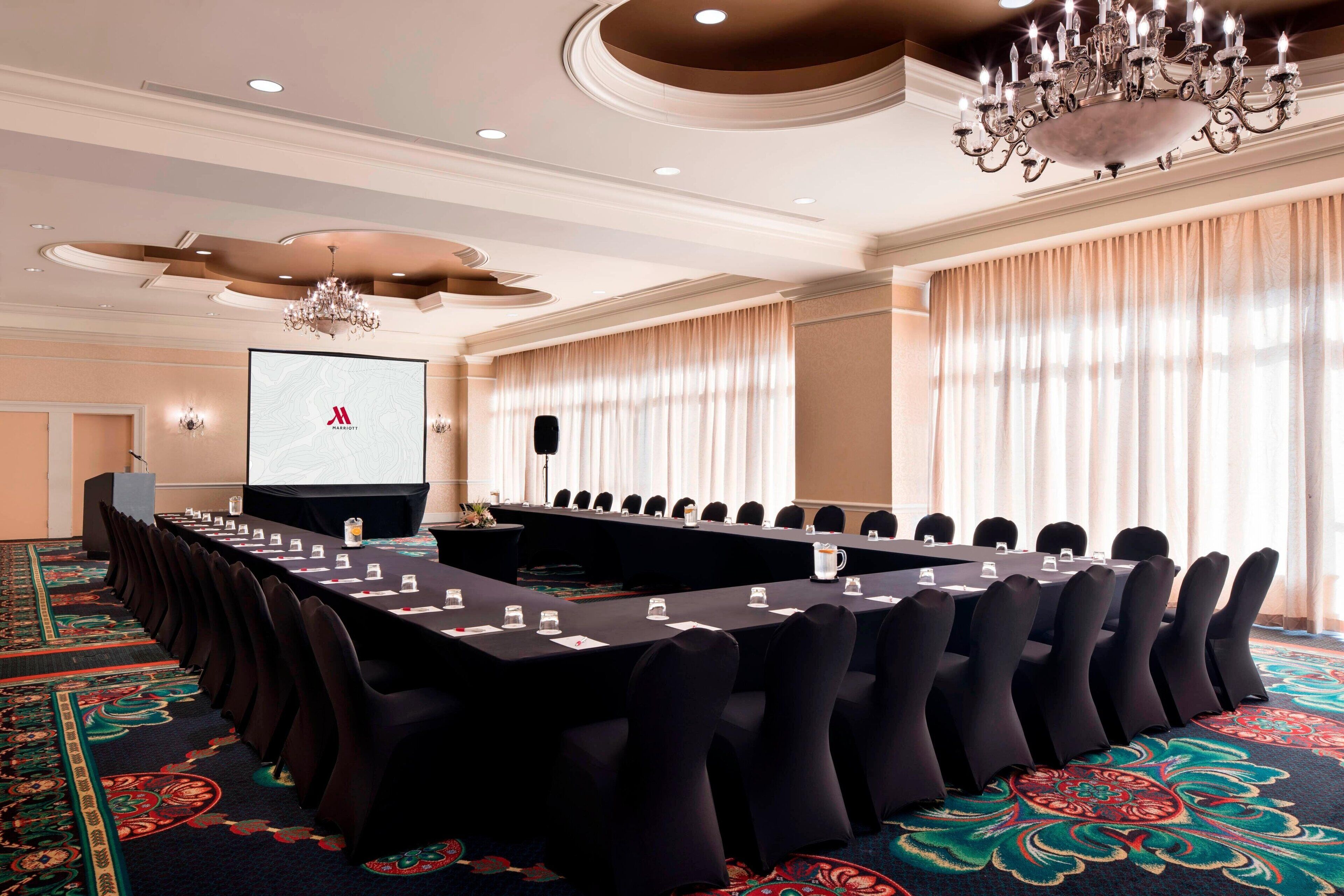A conference room with a long table, chairs, a projector screen, and a chandelier.