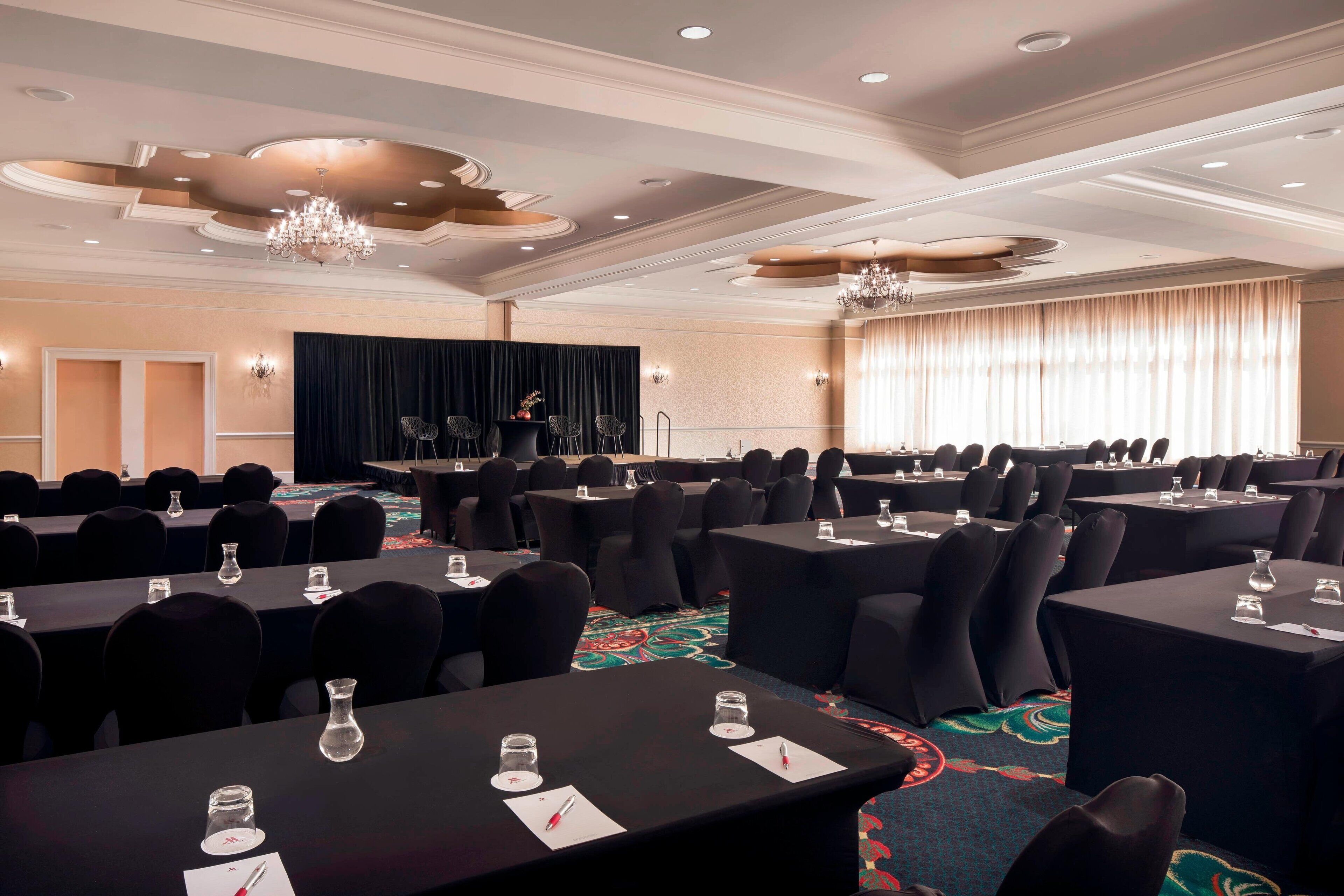 A conference room with multiple tables, chairs, and a stage.