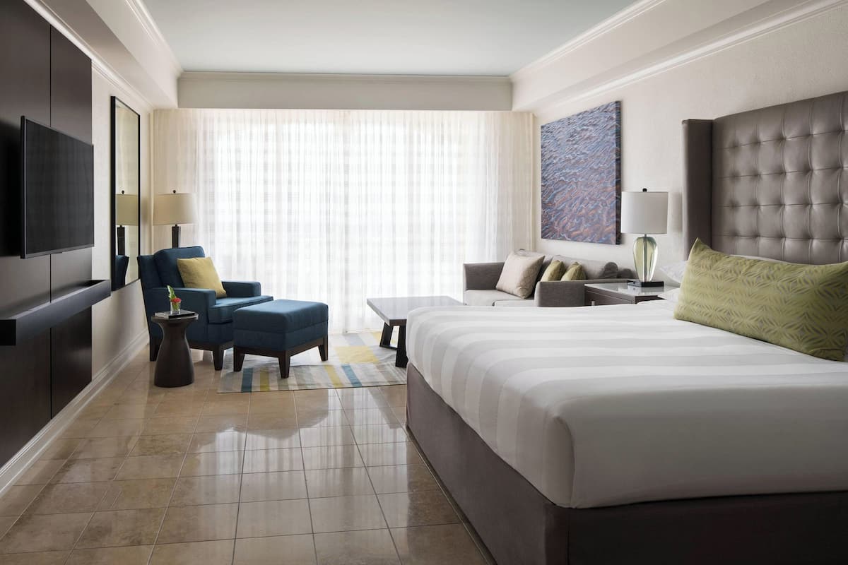 A hotel room with a large bed, a sofa, a chair, a TV, and a window with curtains.