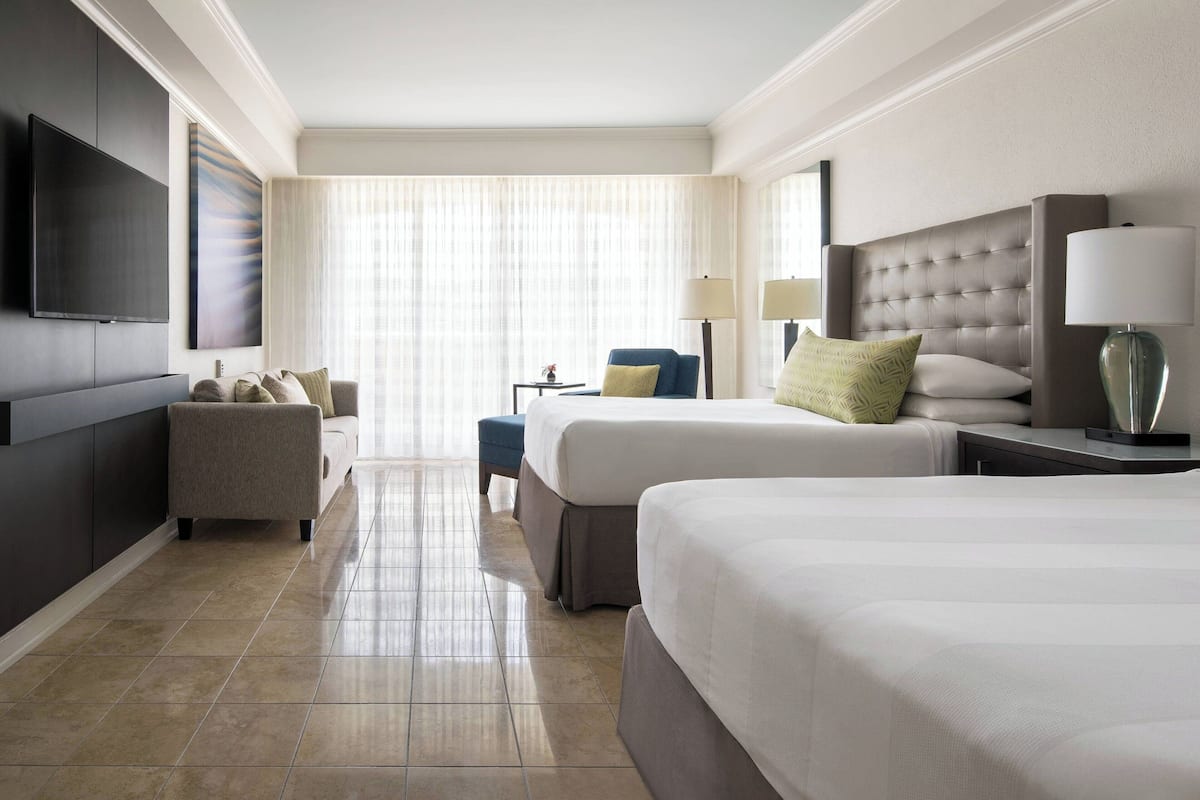 A hotel room with two beds, a sofa, a TV, and a large window with curtains.