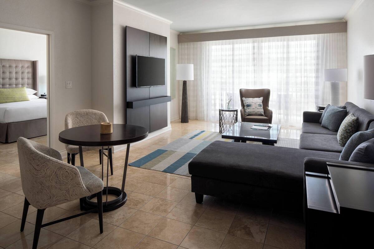 A modern hotel room with a bed, a sofa, a dining area, and a TV.