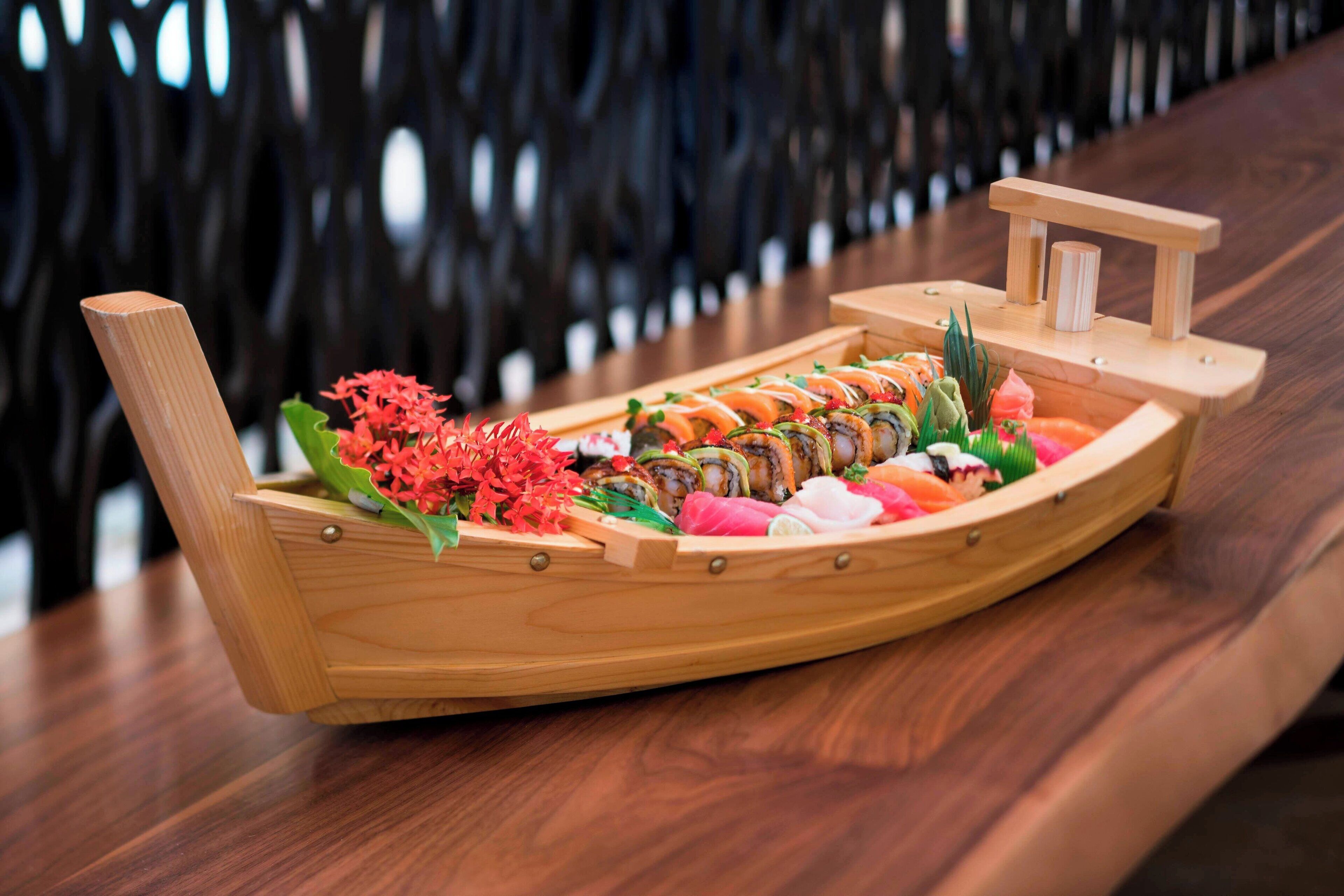 Un plateau de sushis en forme de bateau, fait en bois, posé sur une table.