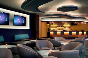 A modern bar area with a curved counter, multiple seating options including sofas and chairs, and a television screen displaying a welcome message.