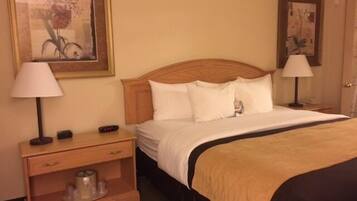 A hotel room with a wooden headboard, a bed with white bedding, a nightstand with a lamp, and a small table with a cup and saucer.