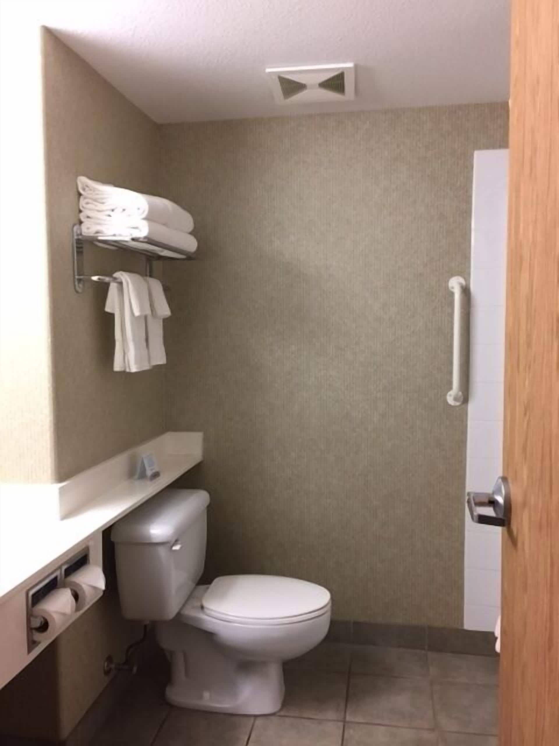 Un baño pequeño con inodoro, un perchero con toallas dobladas y un dispensador de papel higiénico.