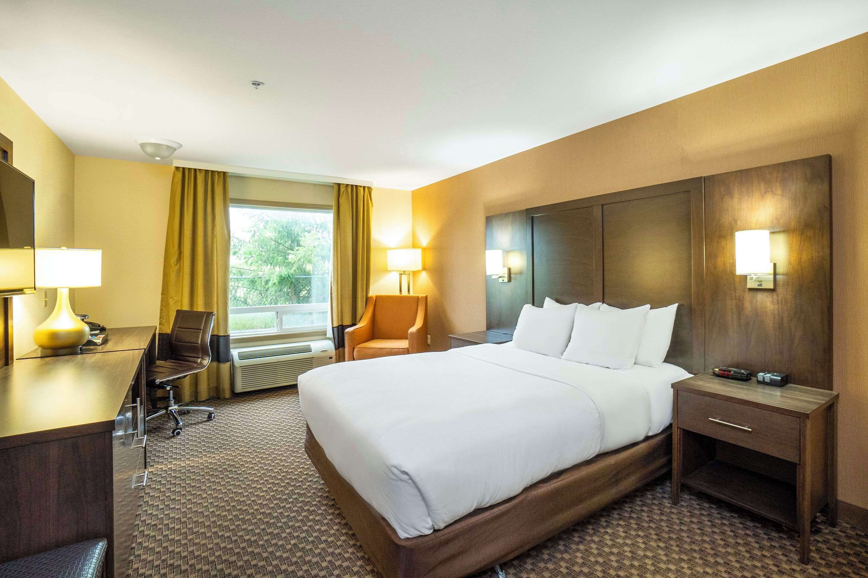 Ein Hotelzimmer mit einem großen Bett, einem Schreibtisch mit Stuhl, einem Nachttisch und einem Fenster mit Vorhängen.