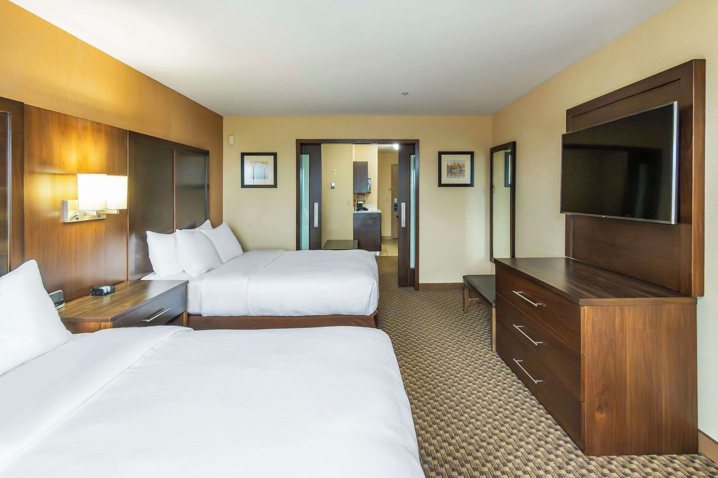 A hotel room with two beds, a dresser, a TV, and a bathroom visible through an open door.