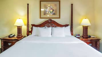 A neatly made bed with a wooden headboard, two bedside tables with lamps, a clock, and a framed floral artwork on the wall.