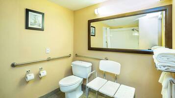 Un baño con inodoro, barras de apoyo, lavamanos, espejo y toallero.