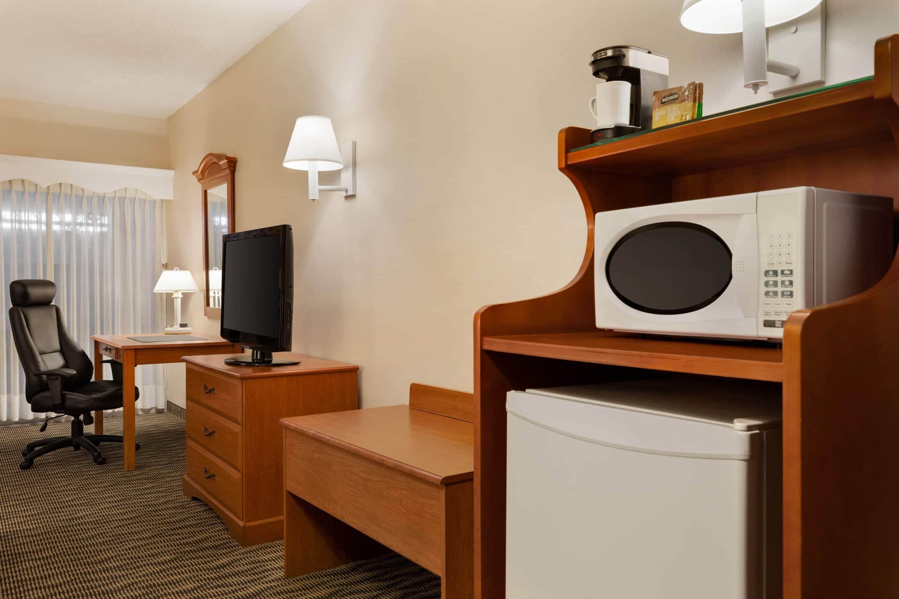 Ein Hotelzimmer mit Schreibtisch, Stuhl, Fernseher, Mikrowelle und Kühlschrank.
