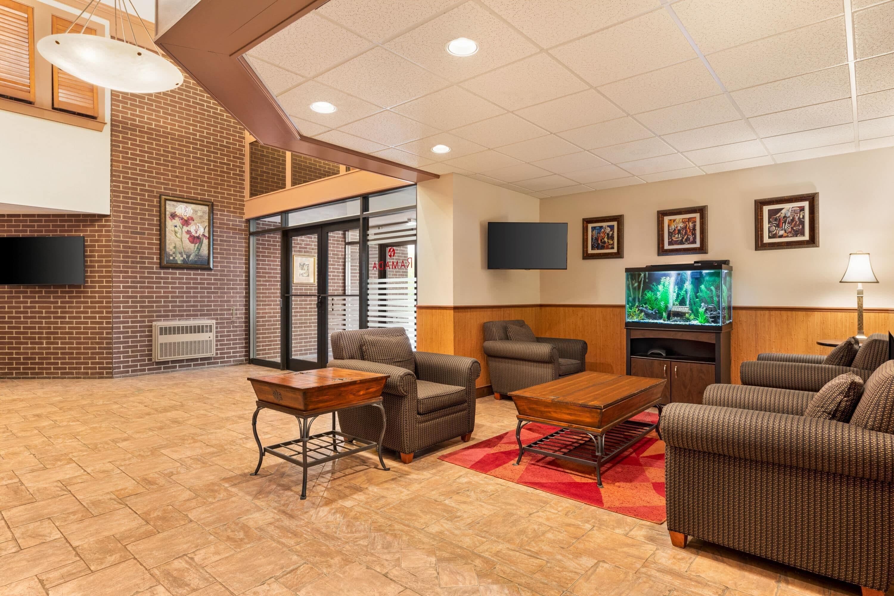 A hotel lobby with brick walls, a fireplace, seating area with sofas and tables, a flat-screen TV, and artwork on the walls.