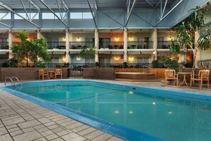 An indoor swimming pool with multiple levels of balconies, each with seating and potted plants. - Ramada by Wyndham Fredericton (Fredericton)