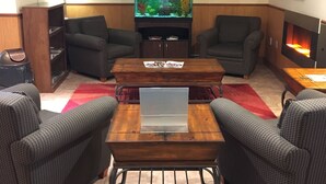A living room with a large fish tank, two armchairs, a coffee table, and a flat-screen TV. - Ramada by Wyndham Fredericton (Fredericton)