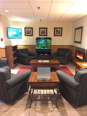A living room with a large fish tank, two armchairs, a coffee table, and a flat-screen TV. - Ramada by Wyndham Fredericton (Fredericton)