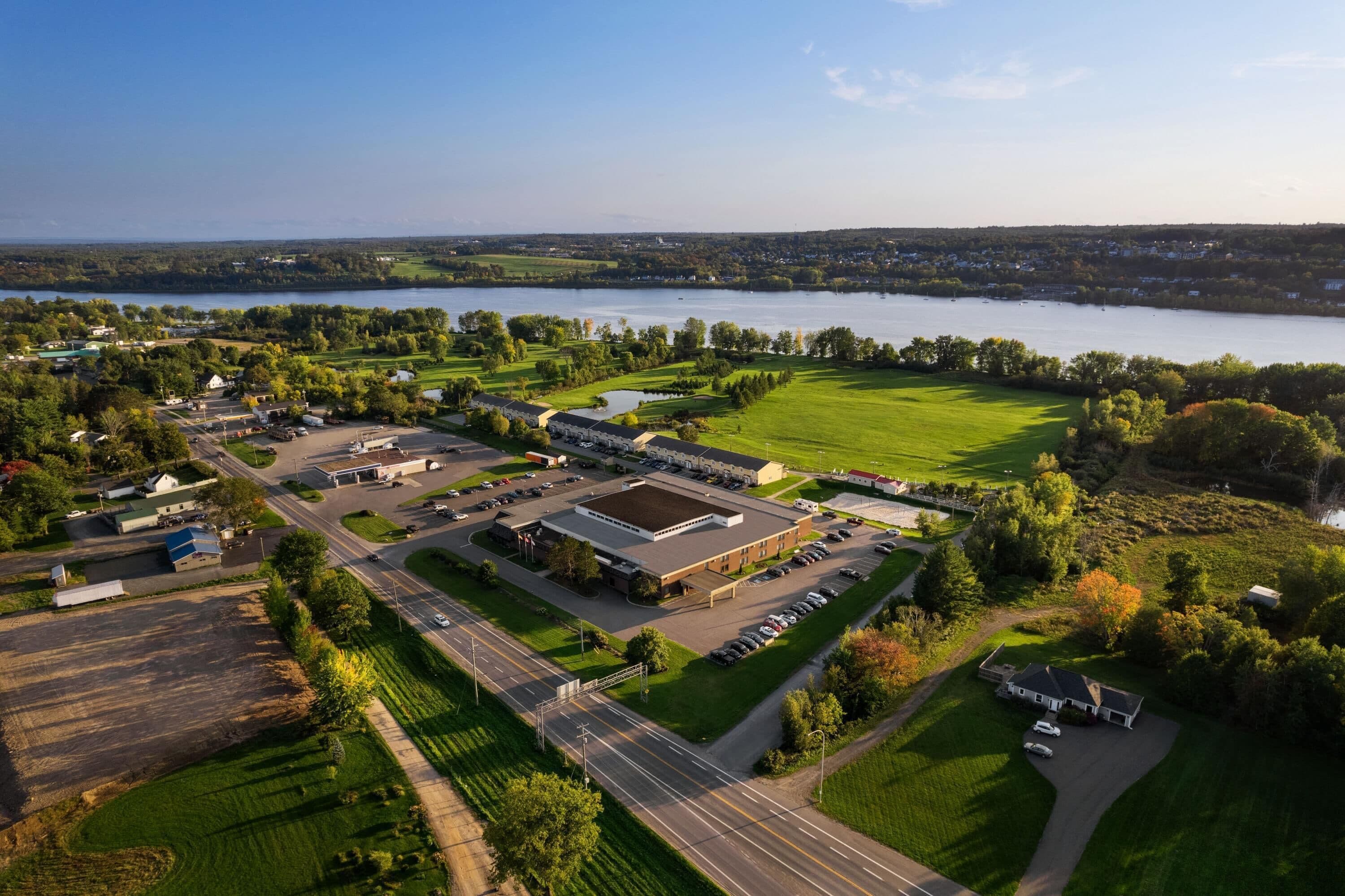 An aerial view of a large complex with multiple buildings, parking areas, and a lake in the background.