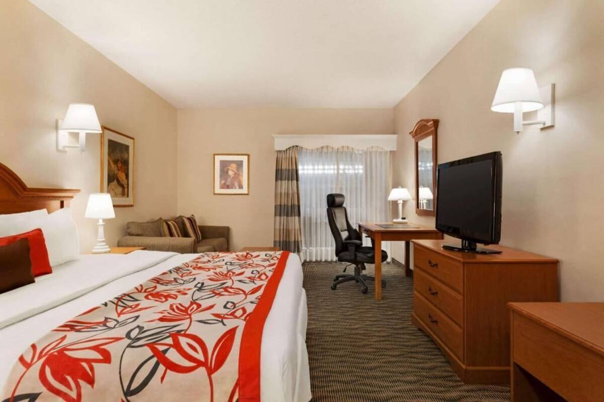 Habitación de hotel con cama, escritorio, silla, televisión y lámparas de pared.