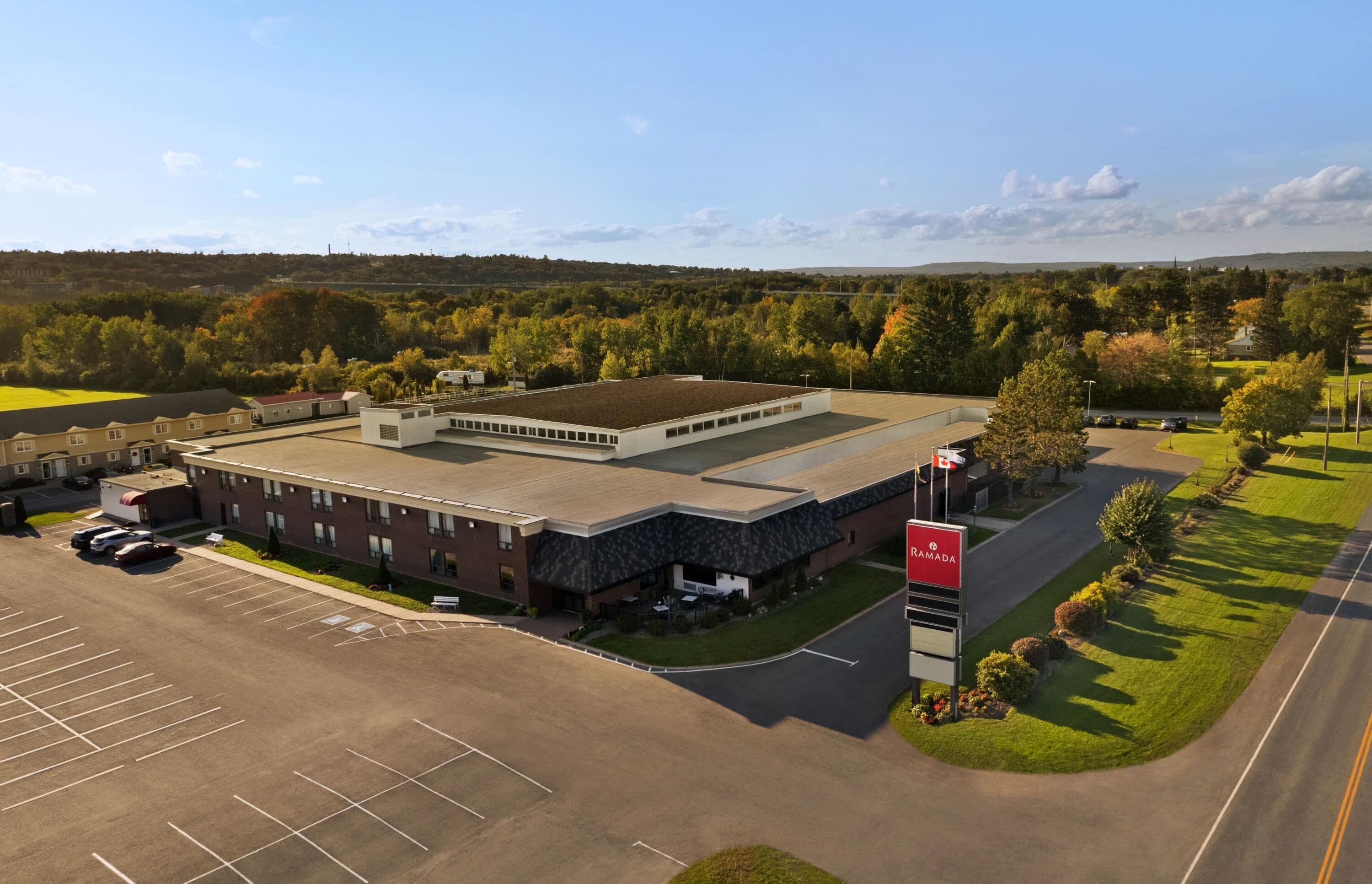 A large building with a parking lot and a sign indicating a Ramada hotel.