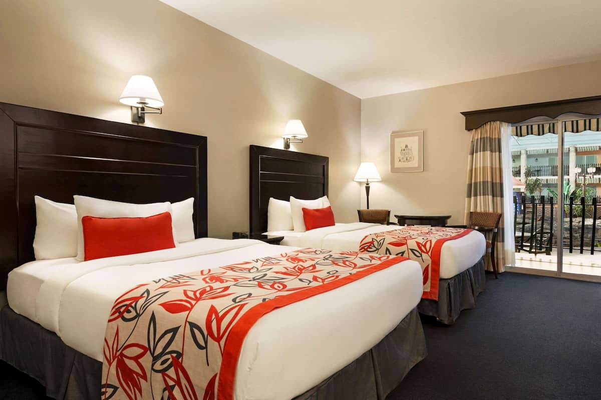 Una habitación de hotel con dos camas, cada una con cabecera, lámparas de noche y una ventana con cortinas.