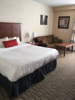 Una habitación de hotel con una cama grande, un sofá, una mesita y una lámpara.