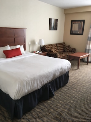 A hotel room with a large bed, a sofa, a small table, and a lamp. - Ramada by Wyndham Fredericton (Fredericton)