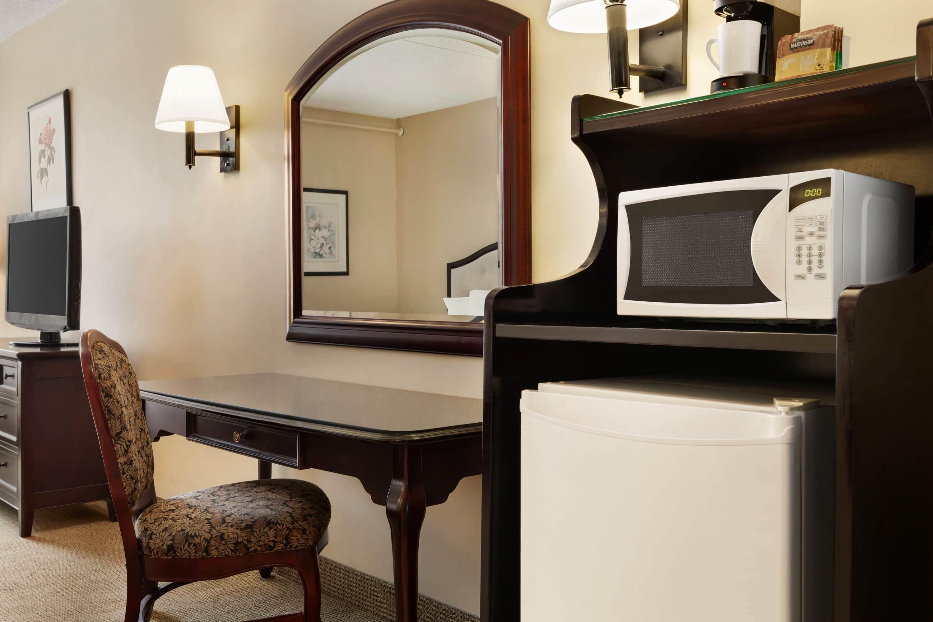 Quarto de hotel com escrivaninha, cadeira, televisão, micro-ondas e frigorífico.