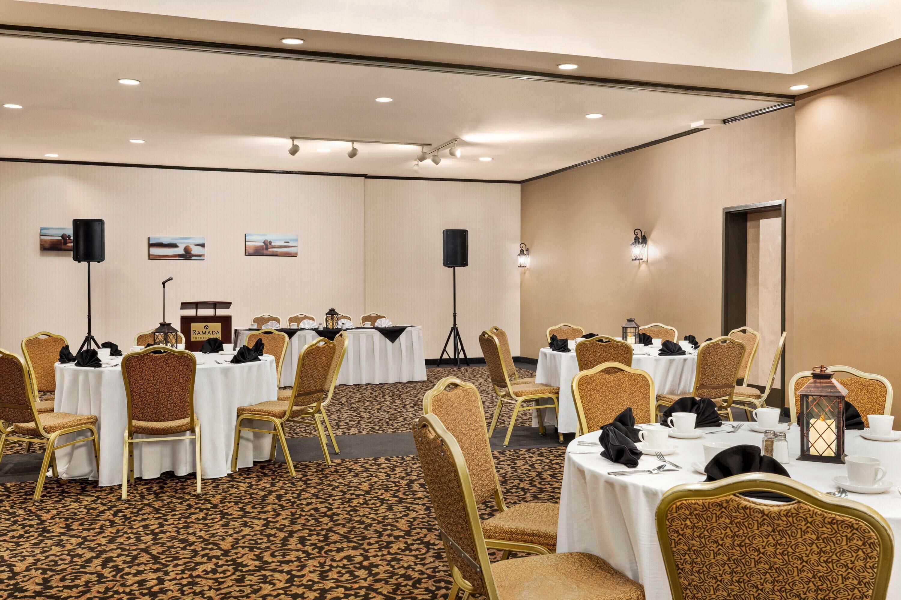 Une salle de conférence avec des tables rondes, des chaises dorées, des nappes blanches et un sol recouvert de moquette.