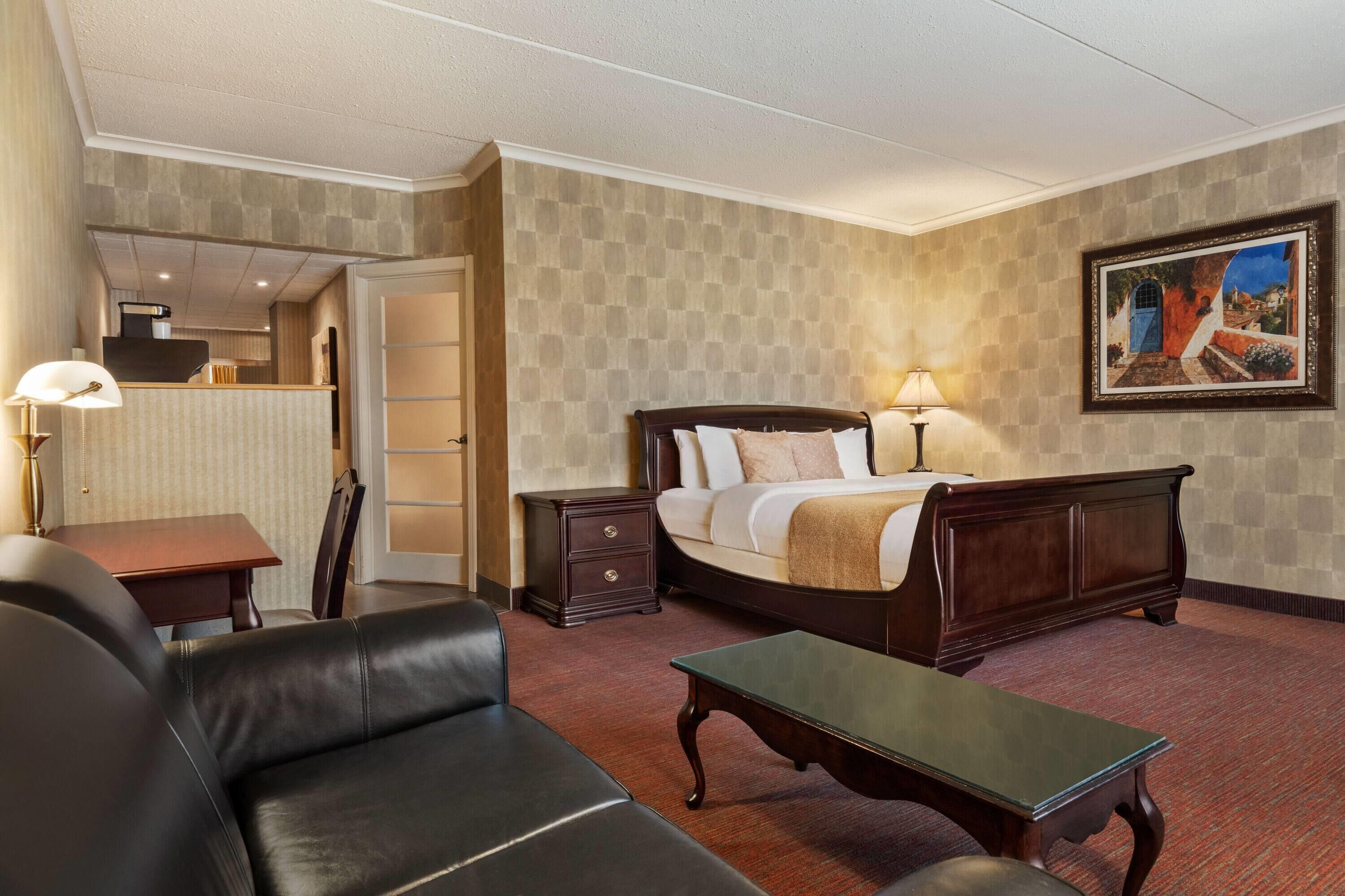 A hotel room with a bed, a desk, a chair, a sofa, and a painting on the wall.