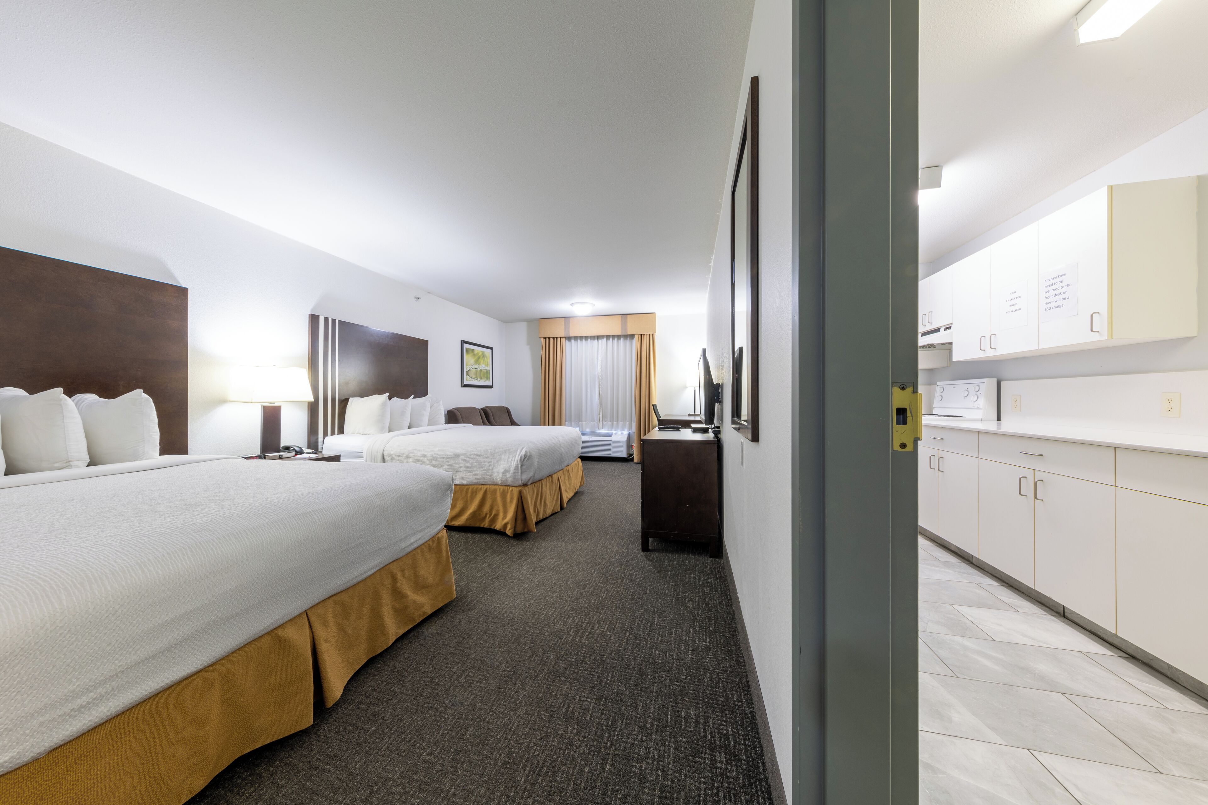 Une chambre d’h ôtel avec deux lits, un bureau et une kitchenette.