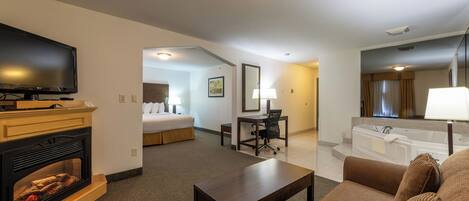A hotel room with a TV, fireplace, sofa, and a bathroom with a bathtub.