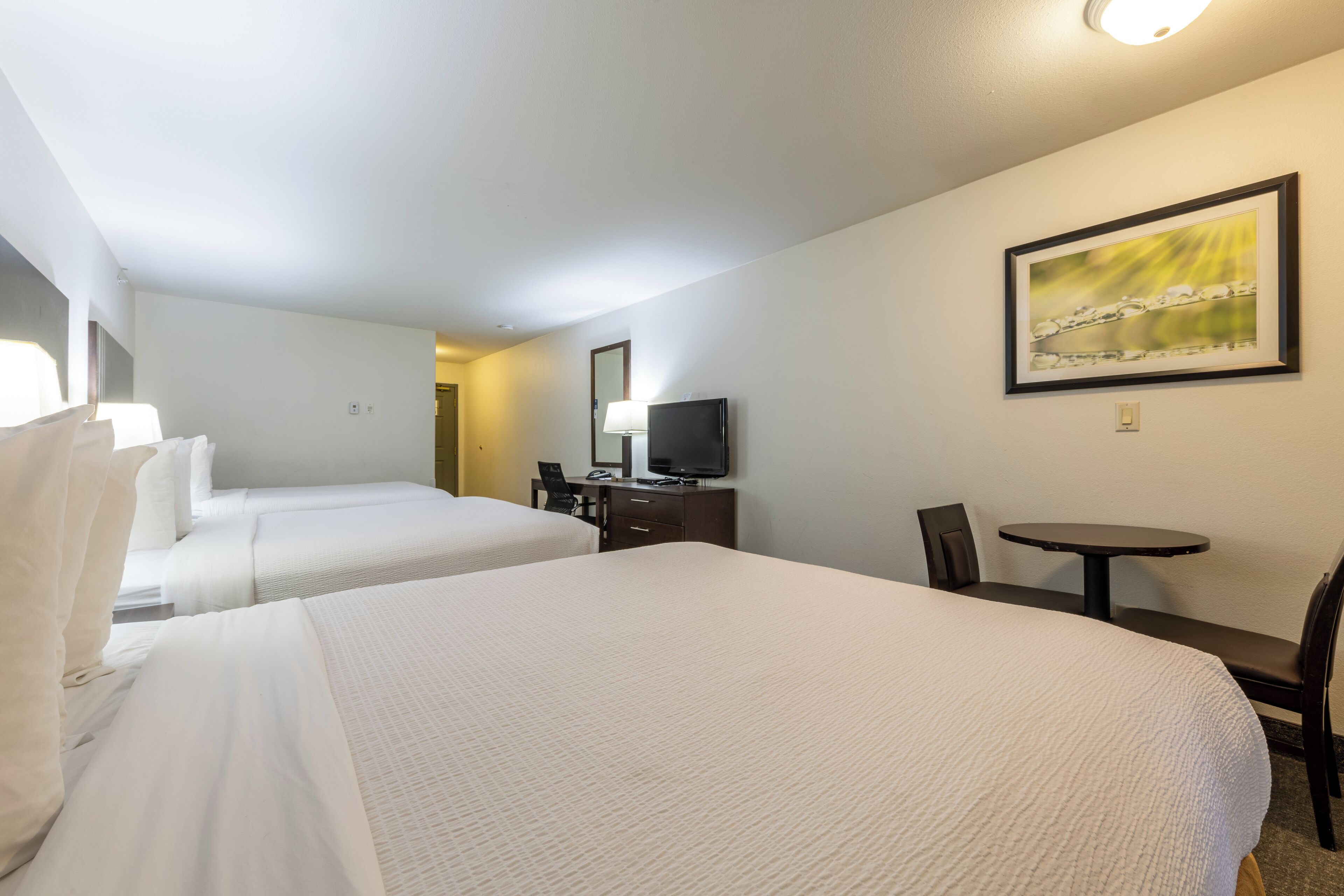 Ein Hotelzimmer mit zwei Betten, einem Schreibtisch, einem Sessel, einem Fernseher und einem Bild an der Wand.