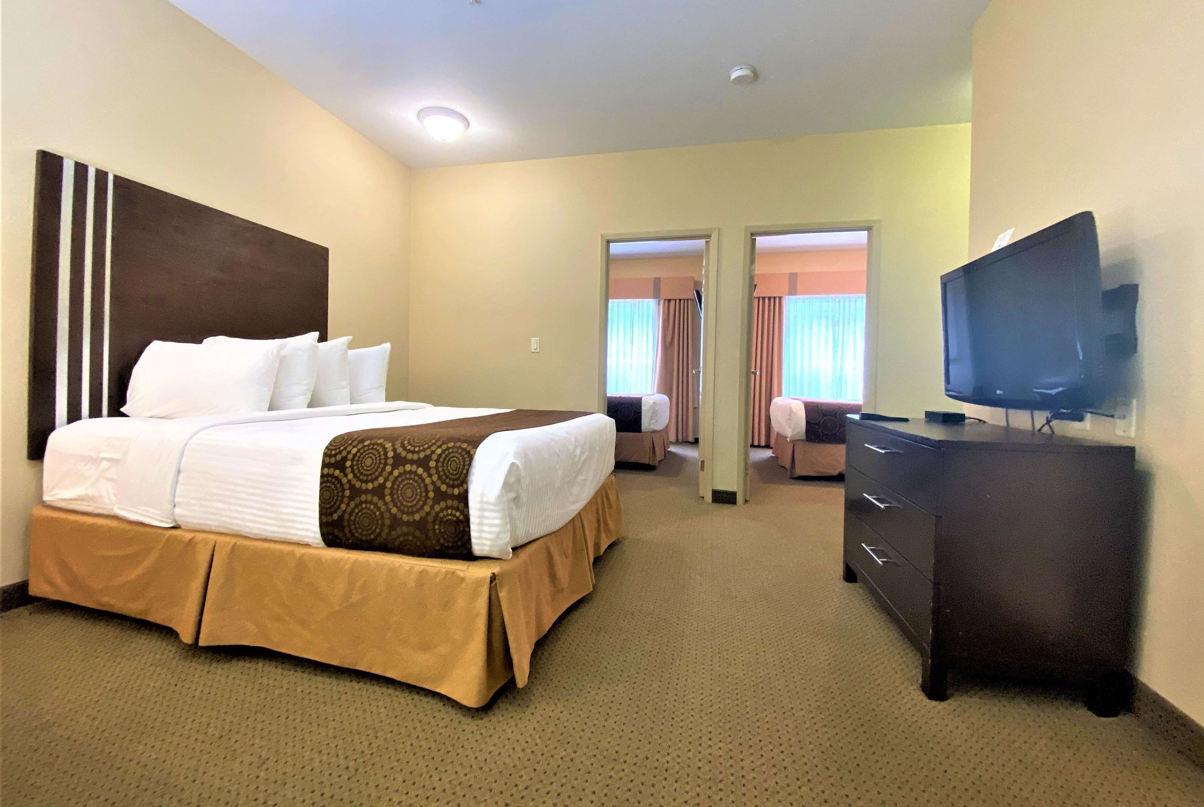 Une chambre d’hôtel avec un grand lit, une commode, une télévision et une porte donnant sur une autre pièce.