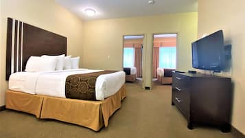 A hotel room with a large bed, a dresser, a television, and a door leading to another room.