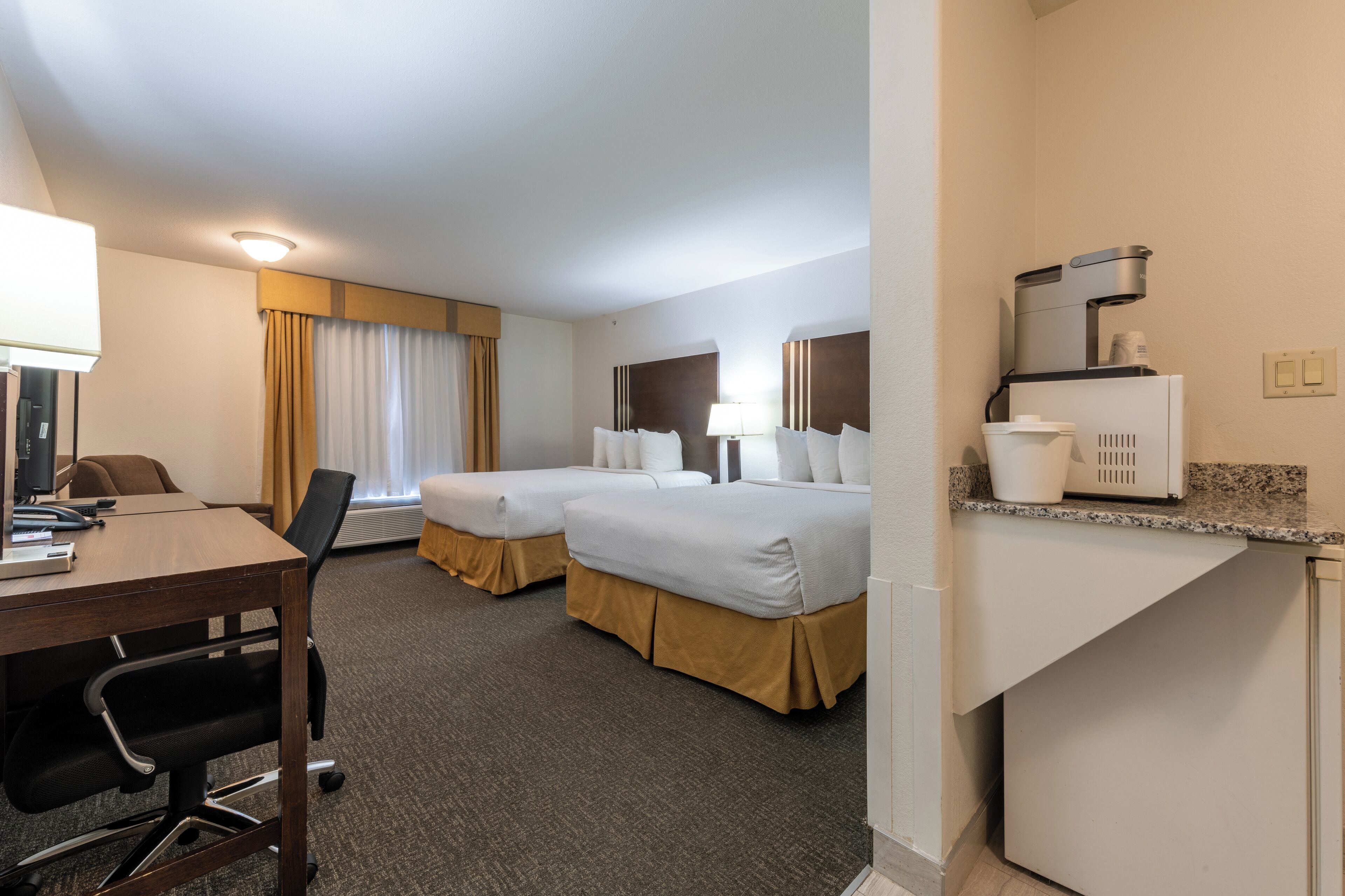 A hotel room with two beds, a desk with a computer, a coffee maker, and a microwave.