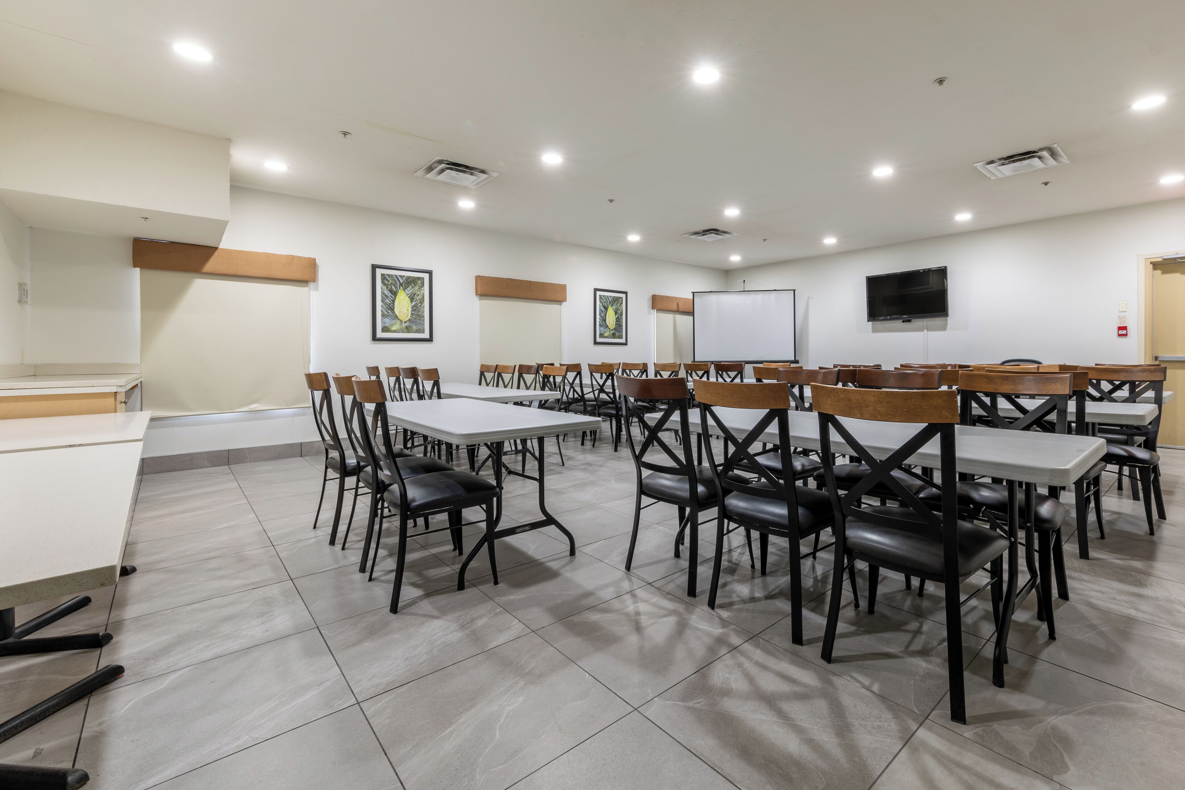 Une salle de conférence dotée de plusieurs tables et chaises, de murs blancs et d’un téléviseur à écran plat fixé au mur.