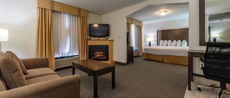 A hotel room with a sofa, a small table, a television, a fireplace, a bed, and a desk with a chair.